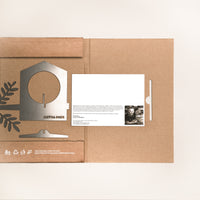 A flat cardboard box displays the Metalbird Canada Bird Feeder kit and a card with text and a photo. Leaf designs and recycling symbols on the box make it perfect for garden art fans.