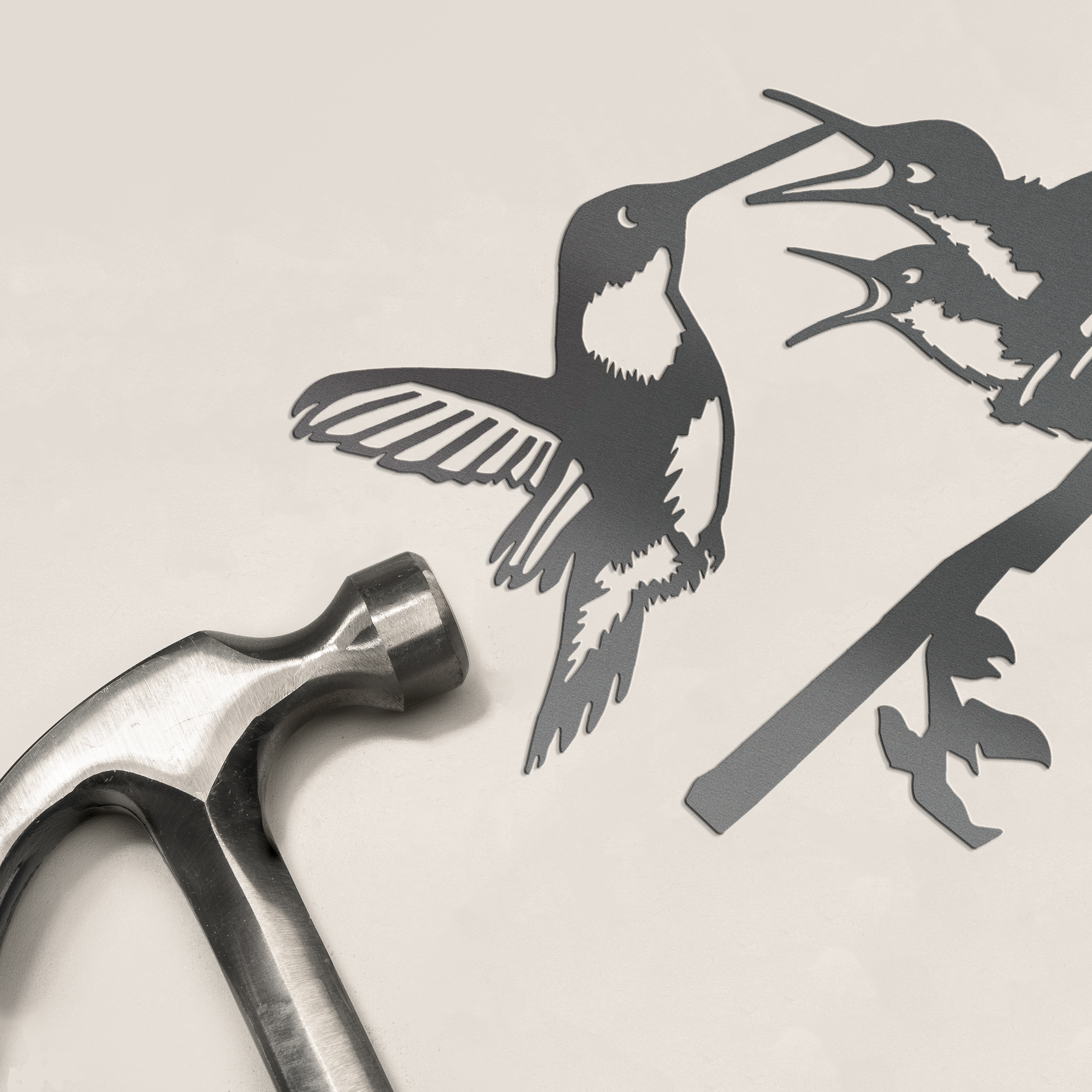 A silver hammer rests beside the limited edition Metalbird Canada "Hummingbird & Chicks" cutout, featuring two hummingbirds on a branch—an ideal Mother's Day gift set against a light background.