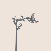 The Hummingbird Plant Stake - 25" by Metalbird Canada features a sleek black corten steel silhouette of a hummingbird drinking from a long-stem flower—an elegant gift for any nature lover.