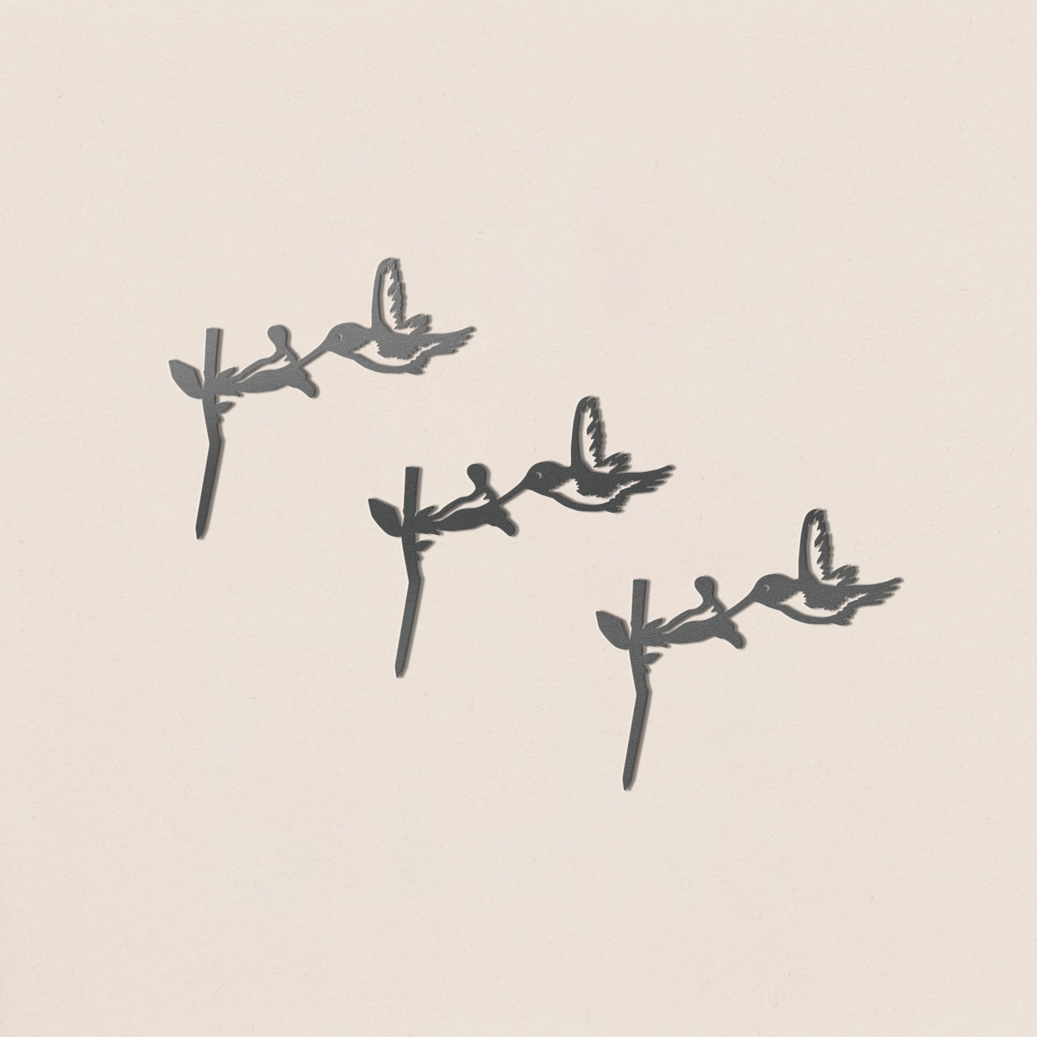 The Baby Bird Bundle - Hummingbird Trio by Metalbird Canada features three hummingbird silhouettes perched on branches in a diagonal arrangement, each casting a unique shadow on a light beige background.