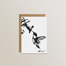 The Metalbird Canada Metalbird Greeting Card Set features a white card with a black silhouette hummingbird and flower design, inspired by metal yard art, paired with a brown envelope against a light backdrop.