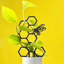 The Honeybee Plant Trellis by Metalbird Canada features a black honeycomb trellis with a metal bee, paired with a green plant in a white ribbed pot against a yellow backdrop—an ideal unique gift.