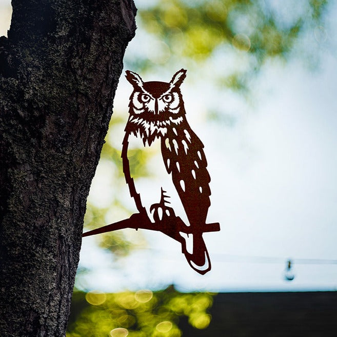 Great Horned Owl steel silhouette mounted beside a tree trunk overlooking water.