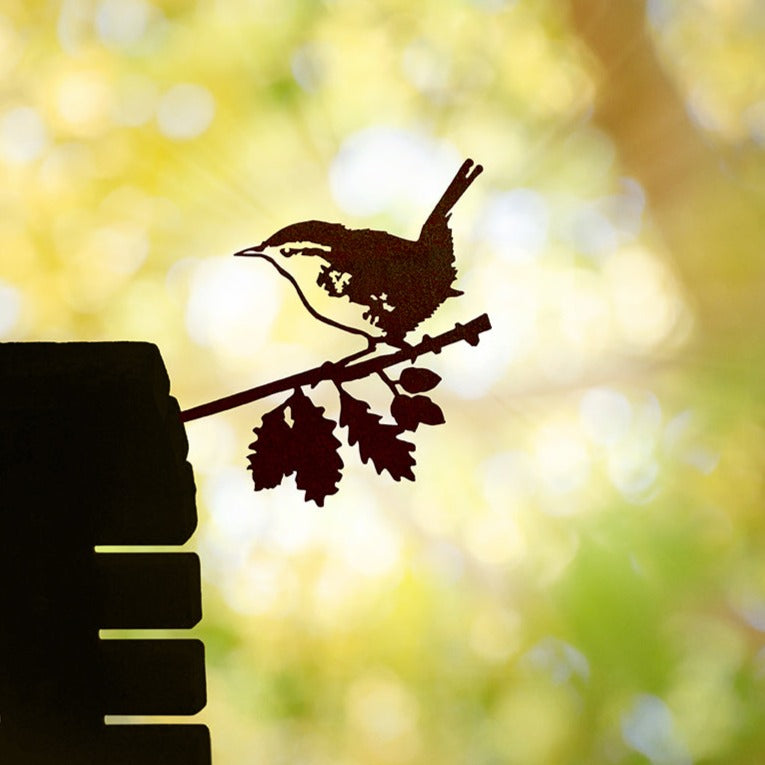 Wren steel silhouette mounted on a wooden post among garden foliage.
