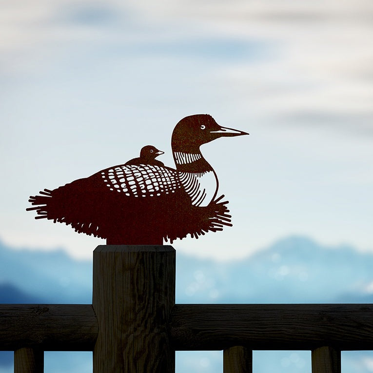 Common Loon and chick steel silhouette mounted on a wooden rail beside a lake.