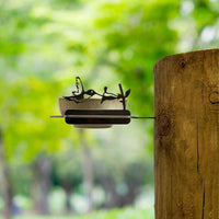 The Metalbird Canada Bowl Feeder, made from corten steel with bird cutout silhouettes and mounted on a wooden post, adds unique yard art to any green outdoor space—an ideal gift for nature lovers.